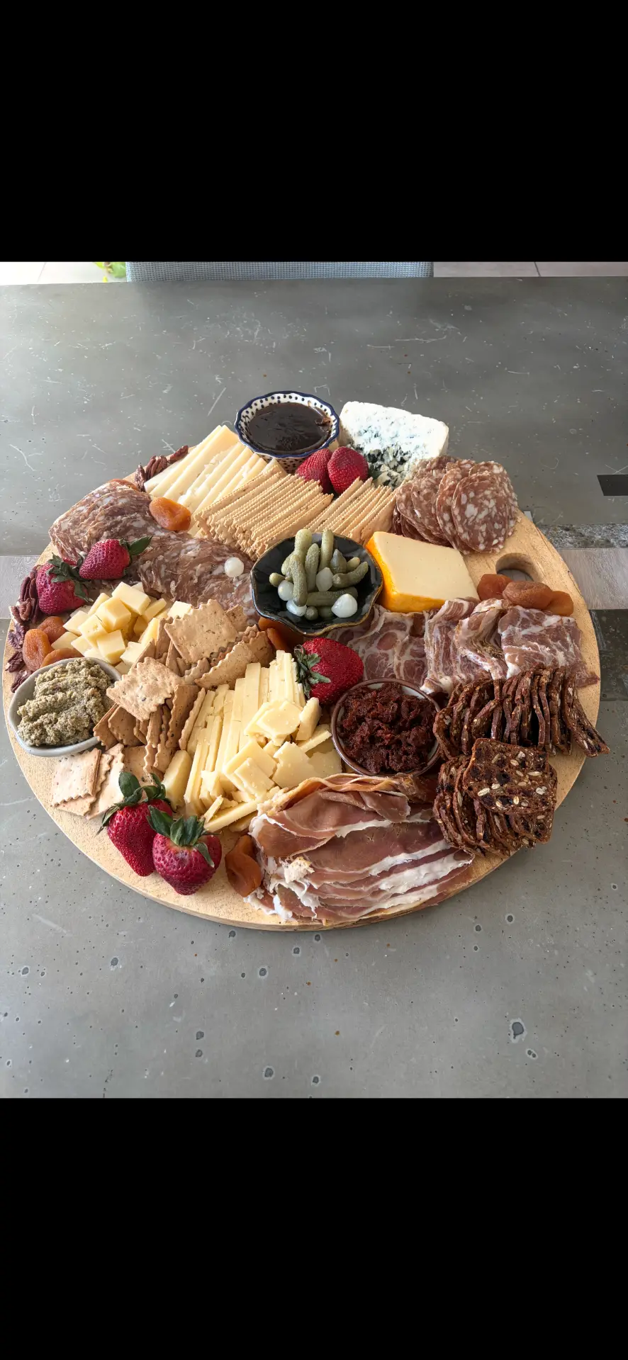 Circular wooden charcuterie board with prosciutto, brie, gouda, strawberries and dried apricots — luxury charcuterie Alaska