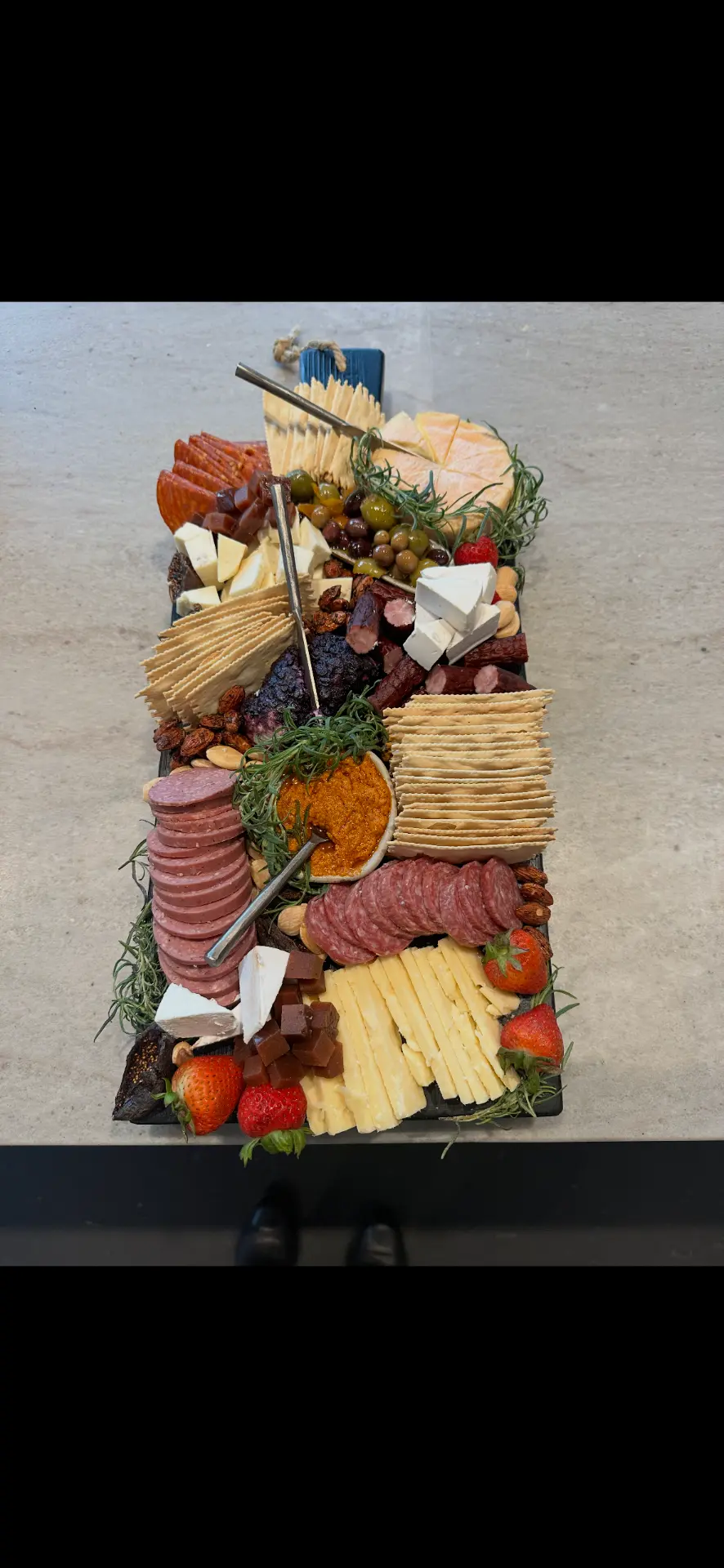 Slate grazing board with summer sausage, chorizo, brie, romesco dip and marinated olives — charcuterie catering Eagle River