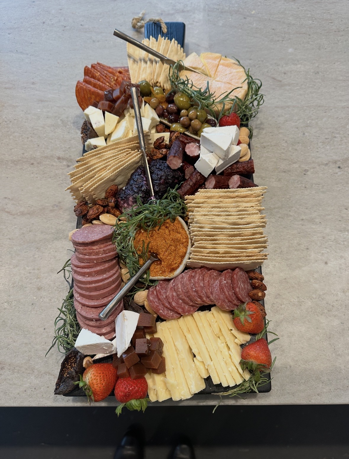 Slate grazing board with summer sausage, chorizo, brie, romesco dip and marinated olives — charcuterie catering Eagle River
